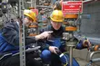 Zwei Industrietechniker mit Schutzhelmen inspizieren und vermessen Anlagen in einem komplexen Rohrsystem, wobei einer auf ein Ventil zeigt.